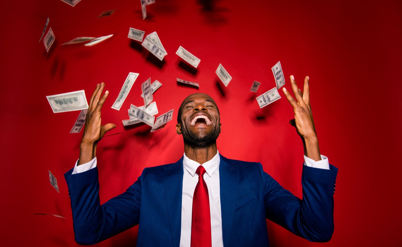 Man in blue suit and red tie laughs as money rains on him