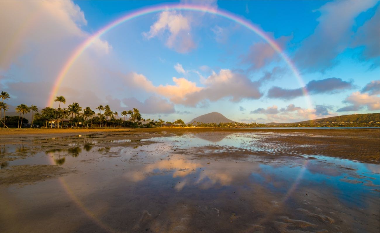 Full circle rainbow across tropical Hawaiian island bay with circle reflections in the ocean water