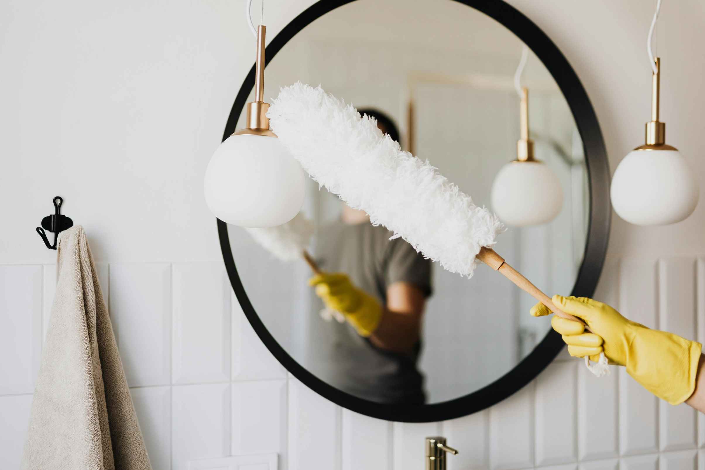 A man using a microfiber feather duster to clean its lamp.