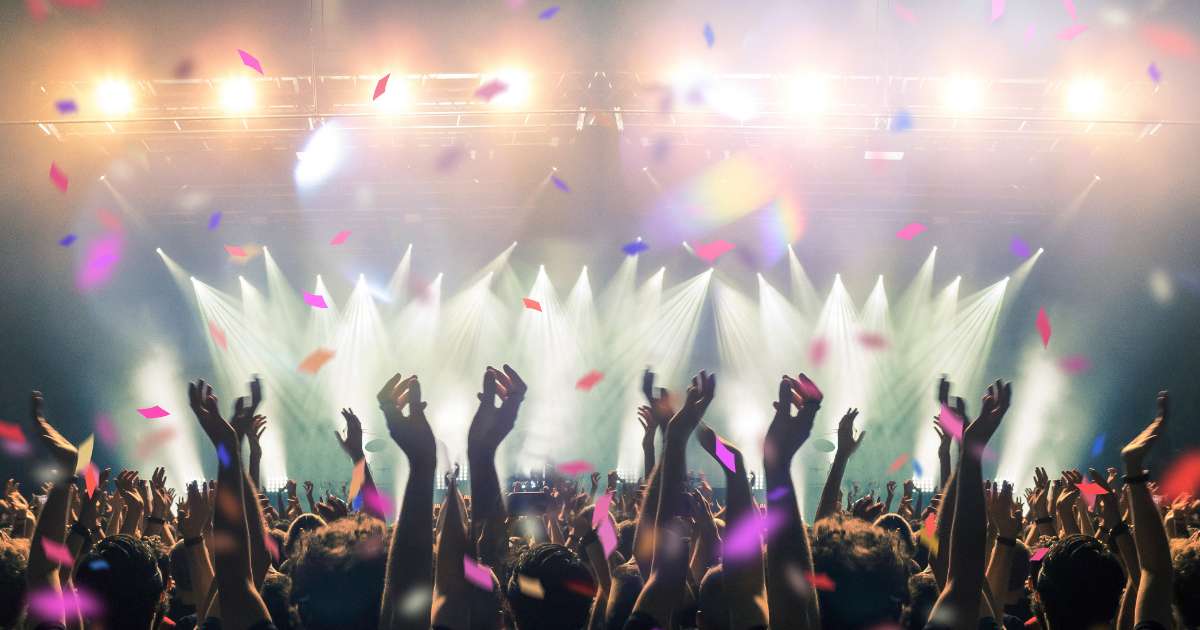 A crowd enjoying a live music festival with raised hands, bright stage lights, and colorful confetti, capturing the energy and atmosphere of summer festivals.
